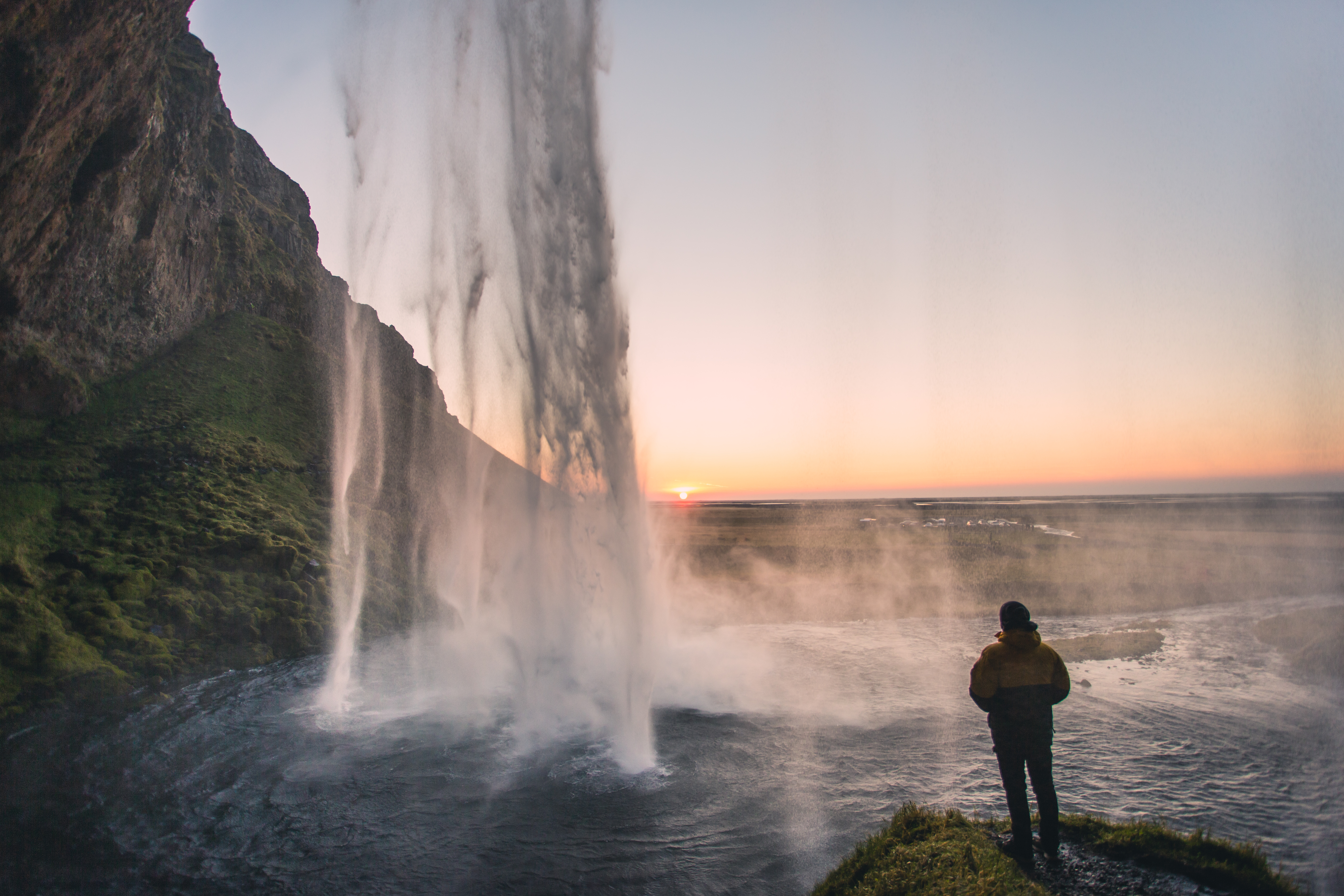 Person standing before a huge waterfall at sunset, golden light pouring through