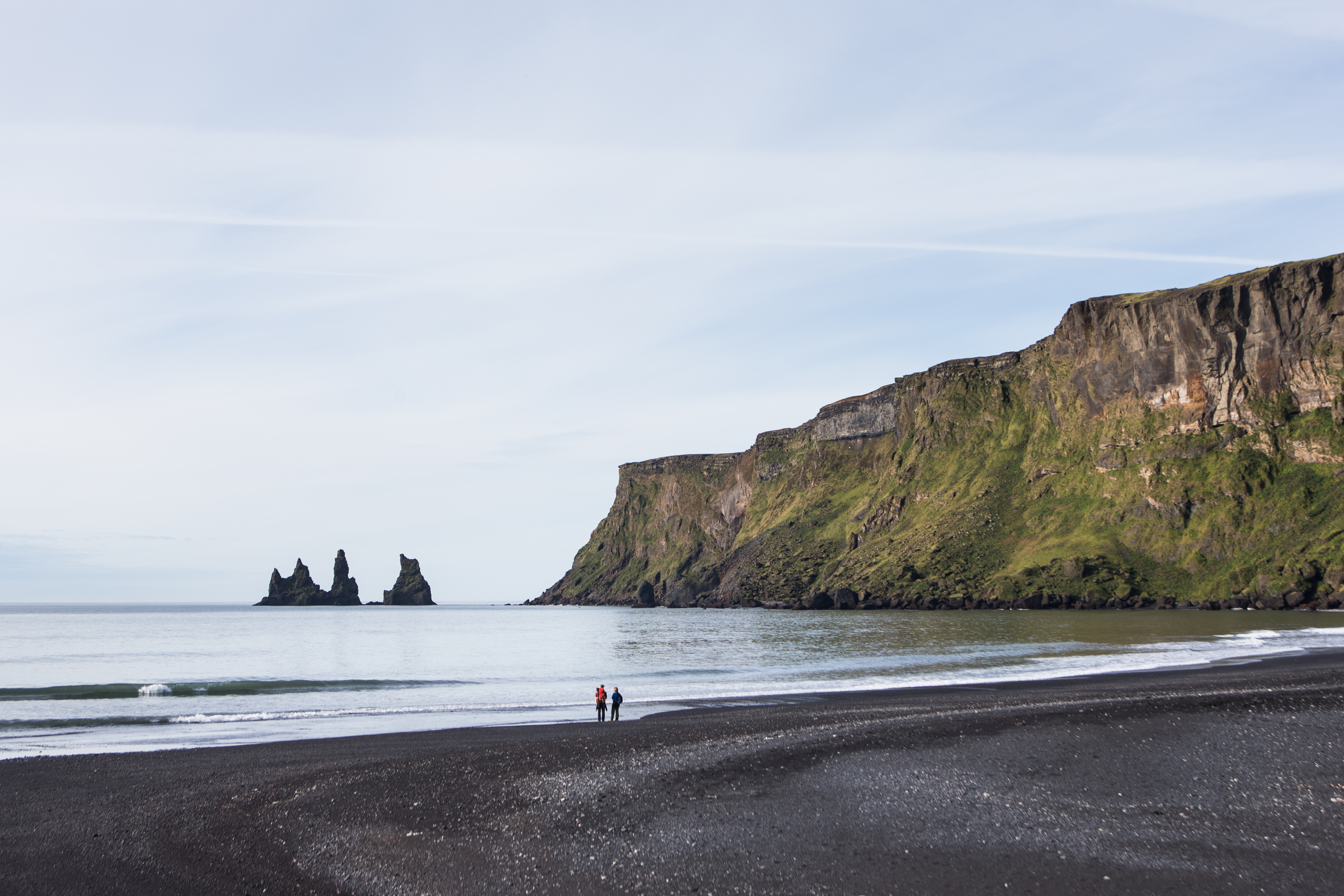 Two tiny figures on a vast black sand beach with sea stacks