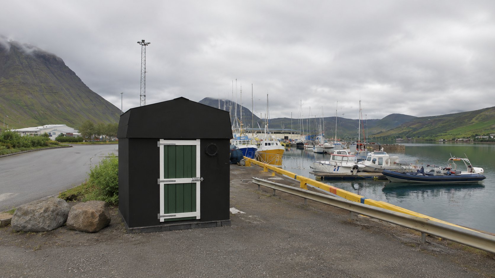 The Iceland Cinema harbour shop — a charming black hut on the quay with fishing boats and mountains behind